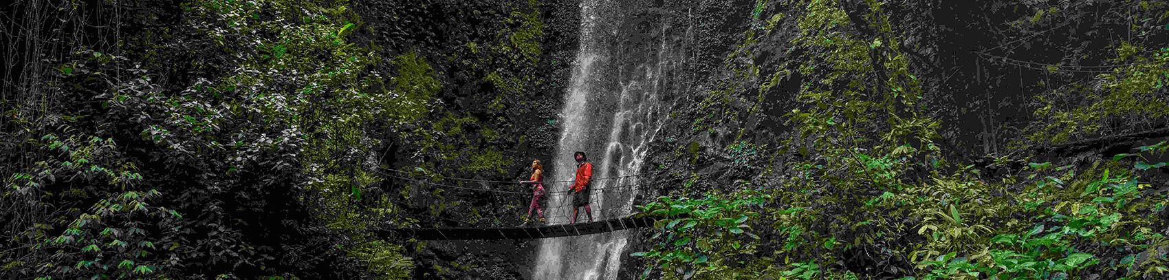 Two people crossing a hanging bridge in front of a stunning waterfall in Monteverde, Costa Rica.