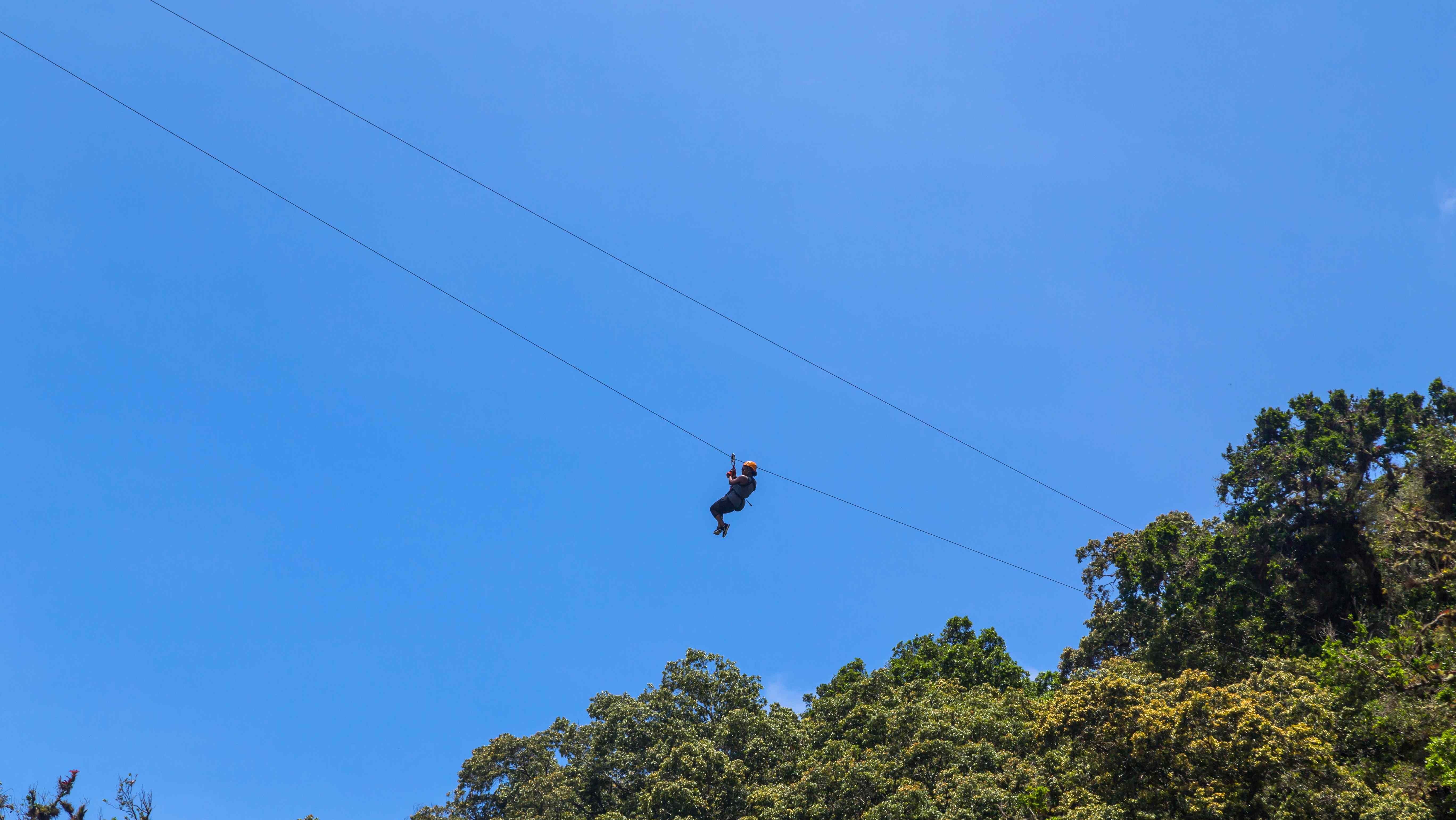 Person ziplining over Monteverde’s cloud forest with a clear blue sky in the background.