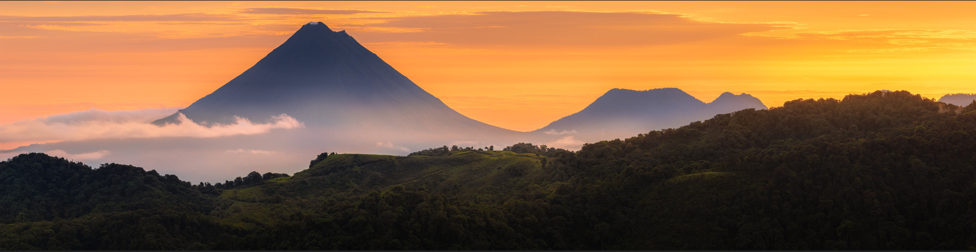  Scenic view of Monteverde’s mountains and volcano with clouds and golden sunset sky