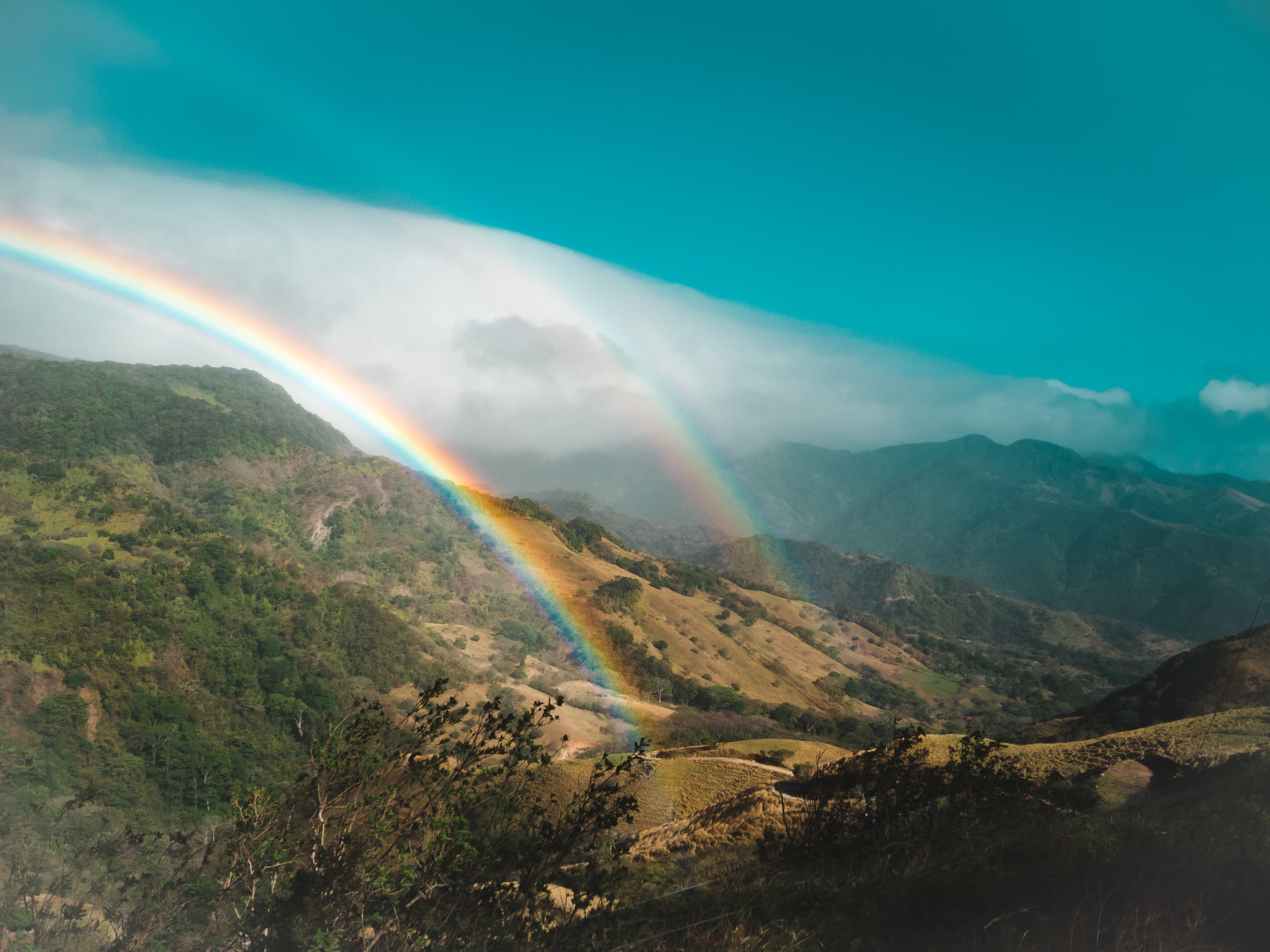 Vibrant rainbow stretching across Monteverde’s green hills during the early rains of the transition season