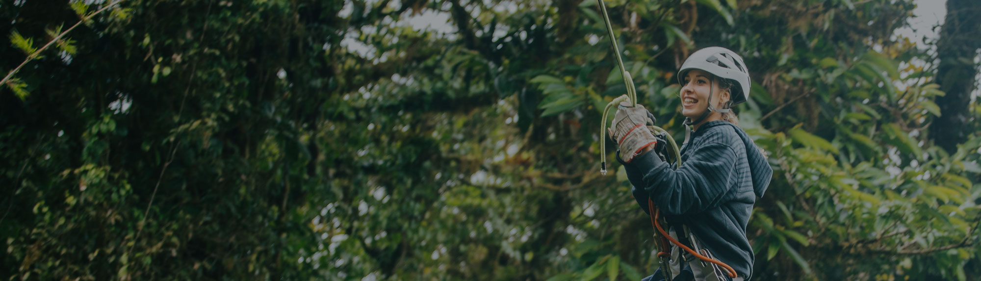 Smiling woman enjoying a canopy tour with a lush forest background in Monteverde, Costa Rica