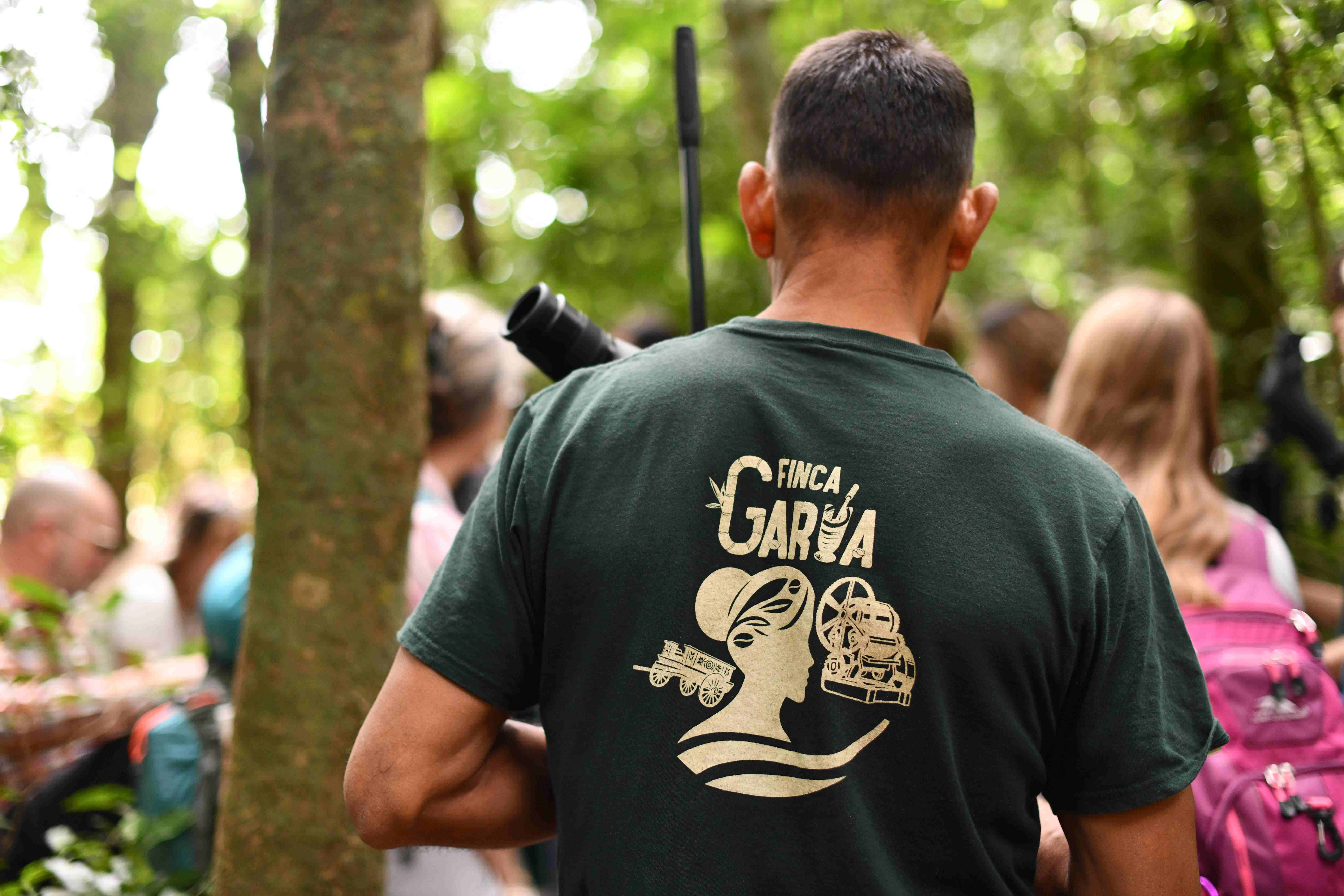 Guía turístico con camiseta verde de Finca Garúa lidera grupo en caminata por bosque tropical.